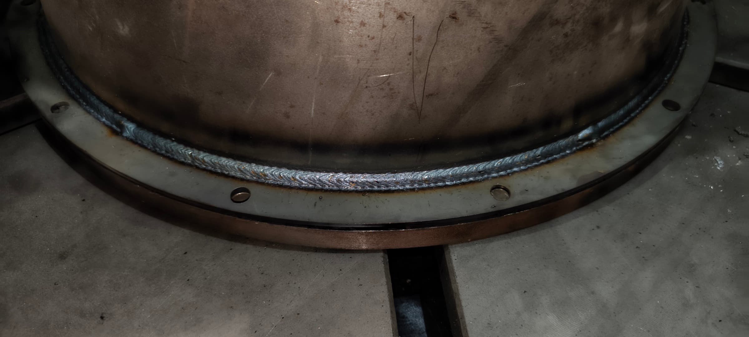 Close-up of a clean, uniform robot weld bead running around a flanged steel vessel